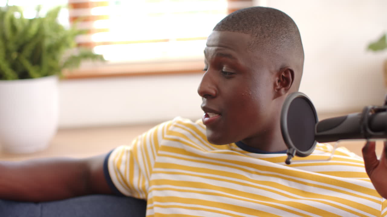 Talking into microphone, african american man in striped shirt recording podcast at home