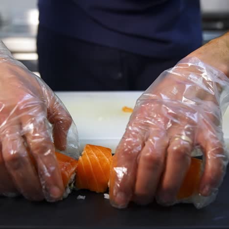 chef in restaurant prepares sushi rolls with salmon, rice and and avocado. cook`s hands putting sushi rolls on the mat. delicious asian food