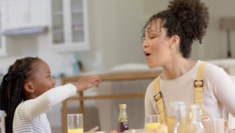 happy african american mother and daughter having breakfast and feeding at home, slow motion