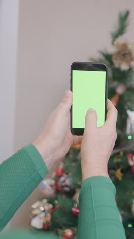 person holding a smartphone with a green screen in front of a christmas tree