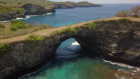 Spectacular-aerial-view-flight-fly-backwards-drone-shot-of-natural-bridge-Broken-Beach-at-Nusa-Penida-in-Bali-Tropical-Island-turquoise-water-waves-rocky-cliffs-Cinematic-above-view-by-Philipp-Marnitz