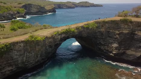 espectacular vista aérea vuelo volar hacia atrás tiro de drone de puente natural playa rota en nusa penida en bali isla tropical olas de agua turquesa acantilados rocosos cinemática vista superior por philipp marnitz