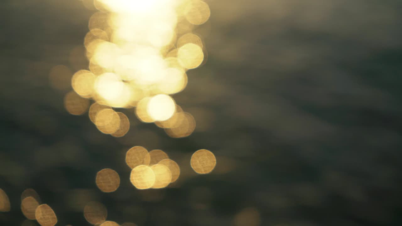 Out of focus footage of sea surface in morning - sun reflects on, creating nice bokeh balls - abstract nature background