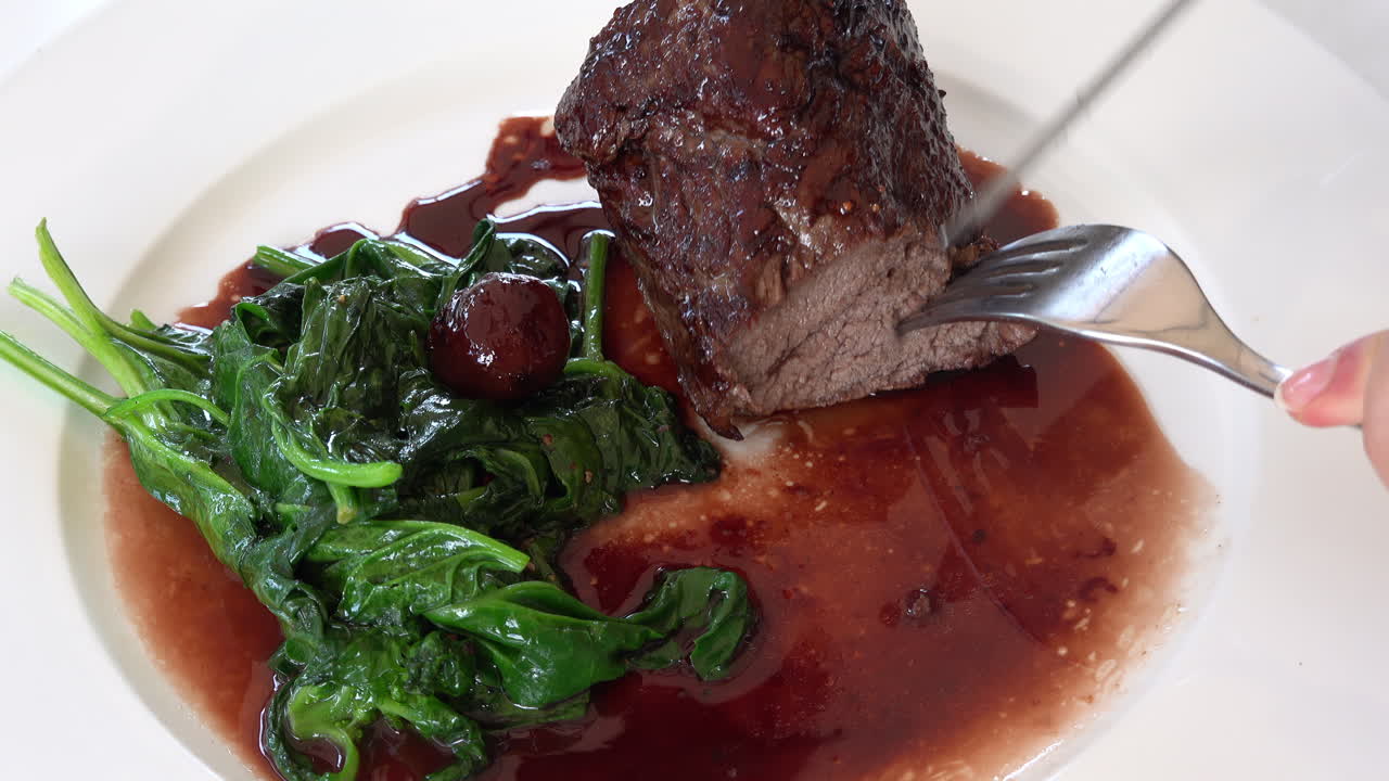 Woman cutting up a cooked beef tenderloin in sauce with greenery on a white plate
