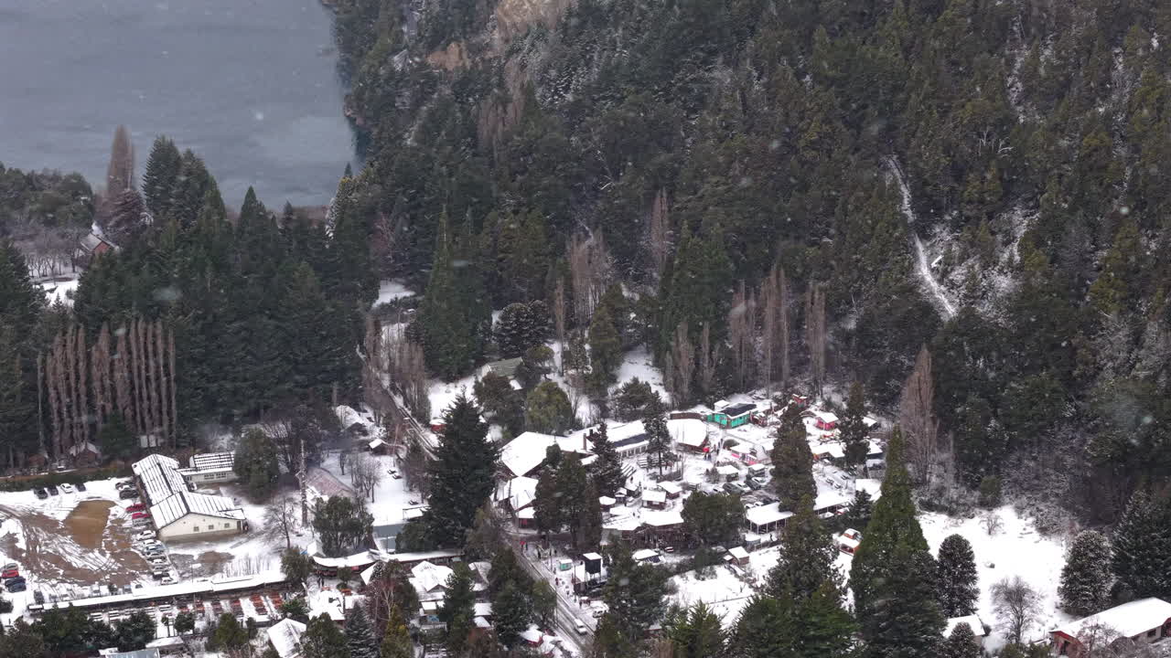 Aerial view of Colonia Suiza settlement with homes and snow-covered ground in mountainous forest terrain, Bariloche, Argentina