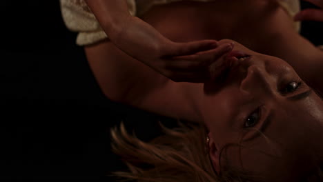 a beautiful woman lies in a dark room and sensually looks at the camera while biting her finger and playfully caressing her body