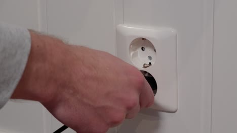 male hand plugging electric cord into 230 volt socket, close up low angle