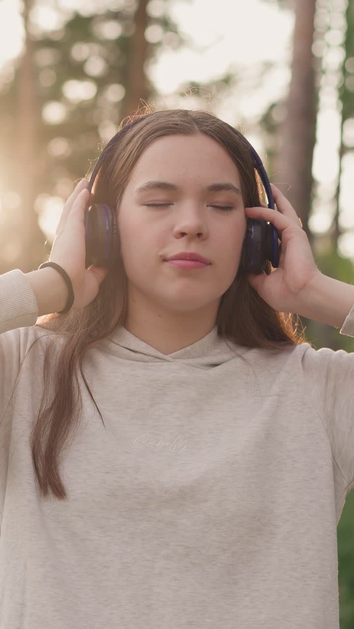 헤드폰을 든 여자가 공원에서 음악을 듣고, 젊은 여자가 여름 해가 지는 동안 은 나무로 둘러싸인 좋아하는 트랙을 즐기고, 자연에서 저녁 기을 느다.