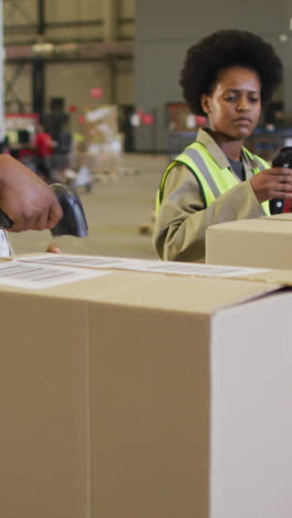 diverse male and female workers wearing safety suits and scanning boxes in warehouse