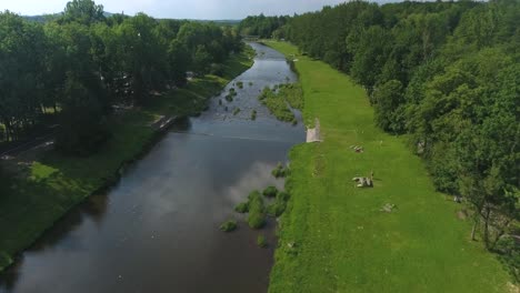 a river flowing through a tourist town during summer, with its banks covered in lush green grass