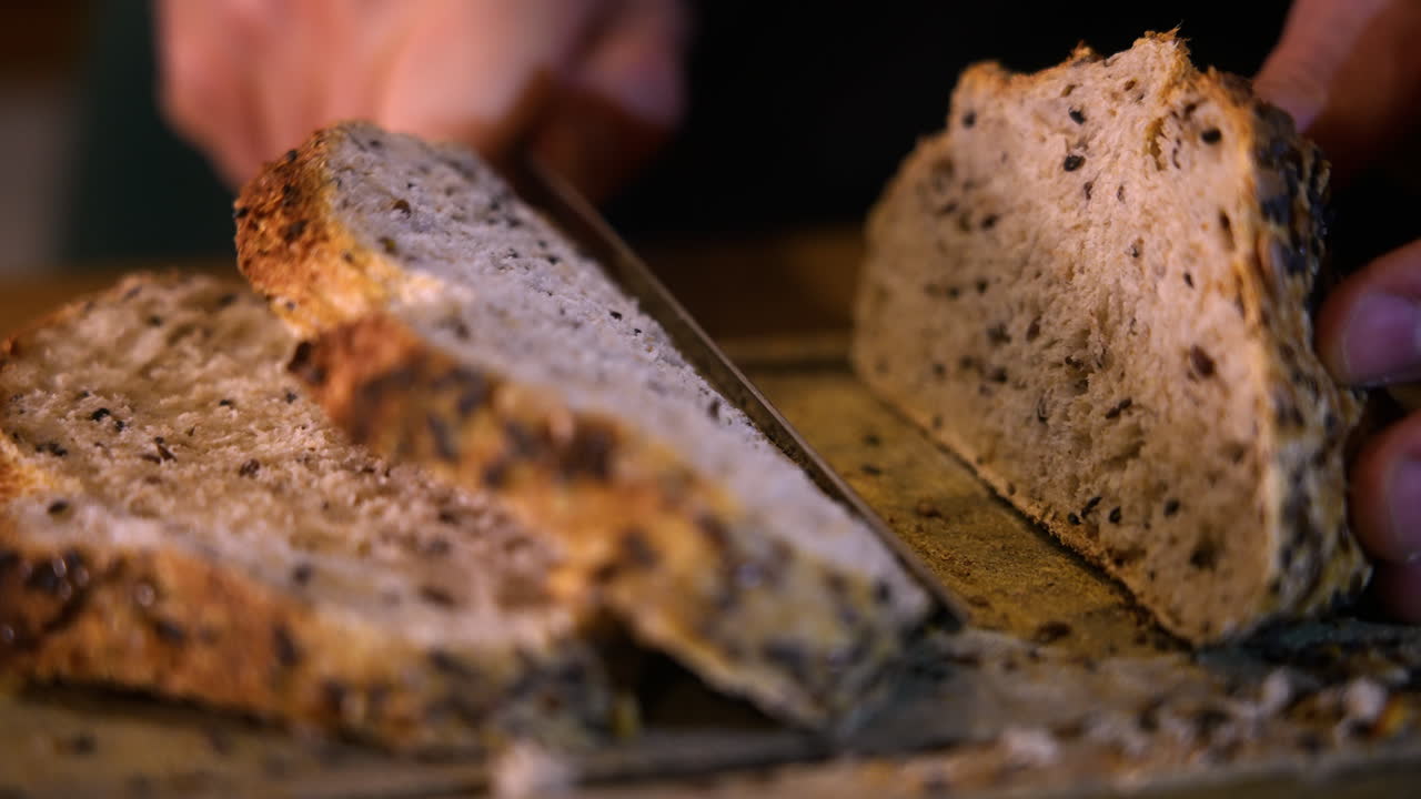 Primo piano delle mani che tagliano pane fresco ai semi su un tagliere