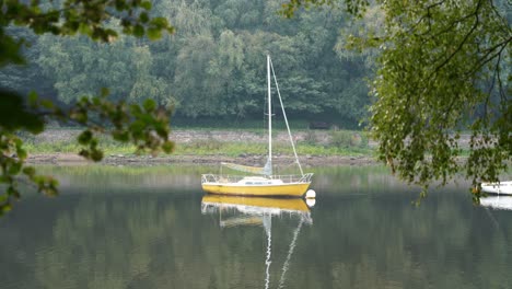 Small-yellow-sailing-yacht-on-a-small-lake-with-calm-still-water,-in-rural-England