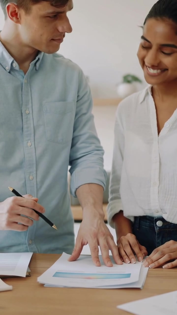 Video verticale: Uomo con camicia blu che indica e cerchia un grafico con una matita a un tavolo di legno, donna che annuisce