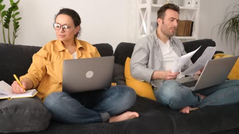 pareja que utiliza computadoras portátiles para el trabajo remoto en el sofá en casa, cónyuges enfocados que trabajan a distancia