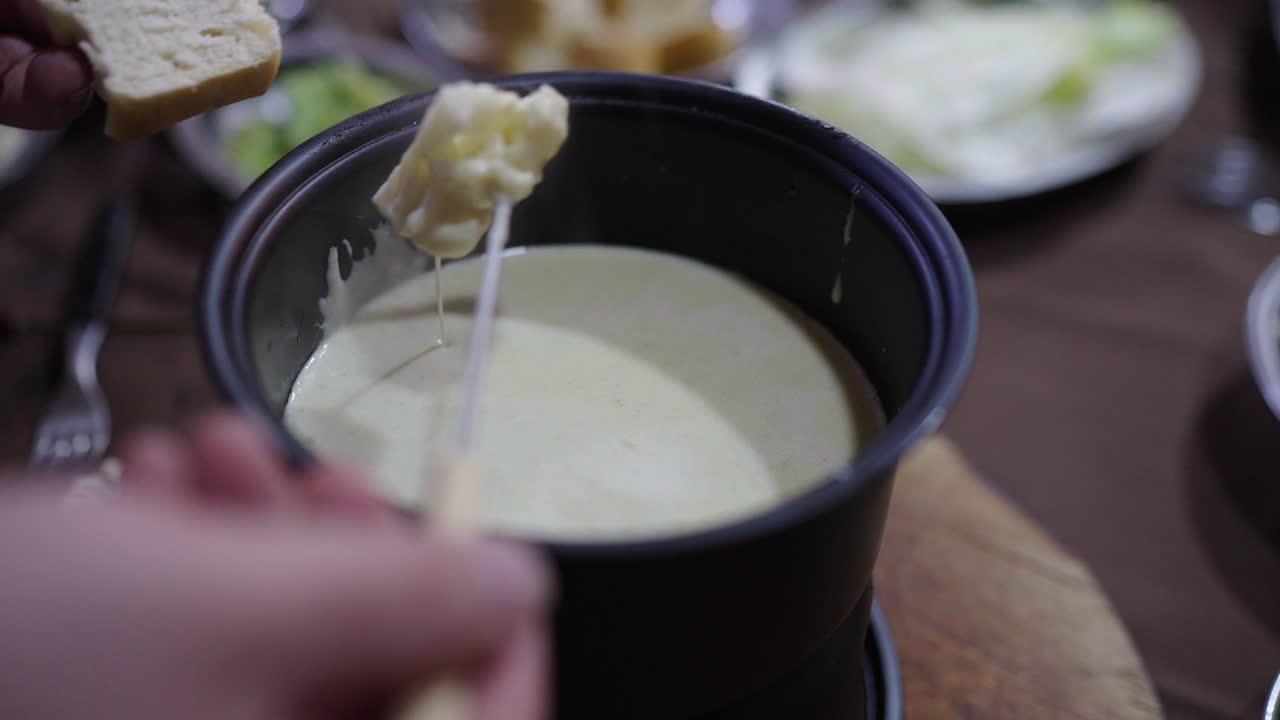 Hand prepares to dip a piece of rustic bread into a hot pan of Bagna Cauda sauce, made with anchovies, garlic, olive oil, and butter, served warm during a traditional Piedmontese gathering.