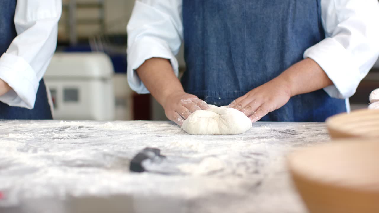 Vertical video: Female baker picking up dough end, folding and pinching on floured bench for baking