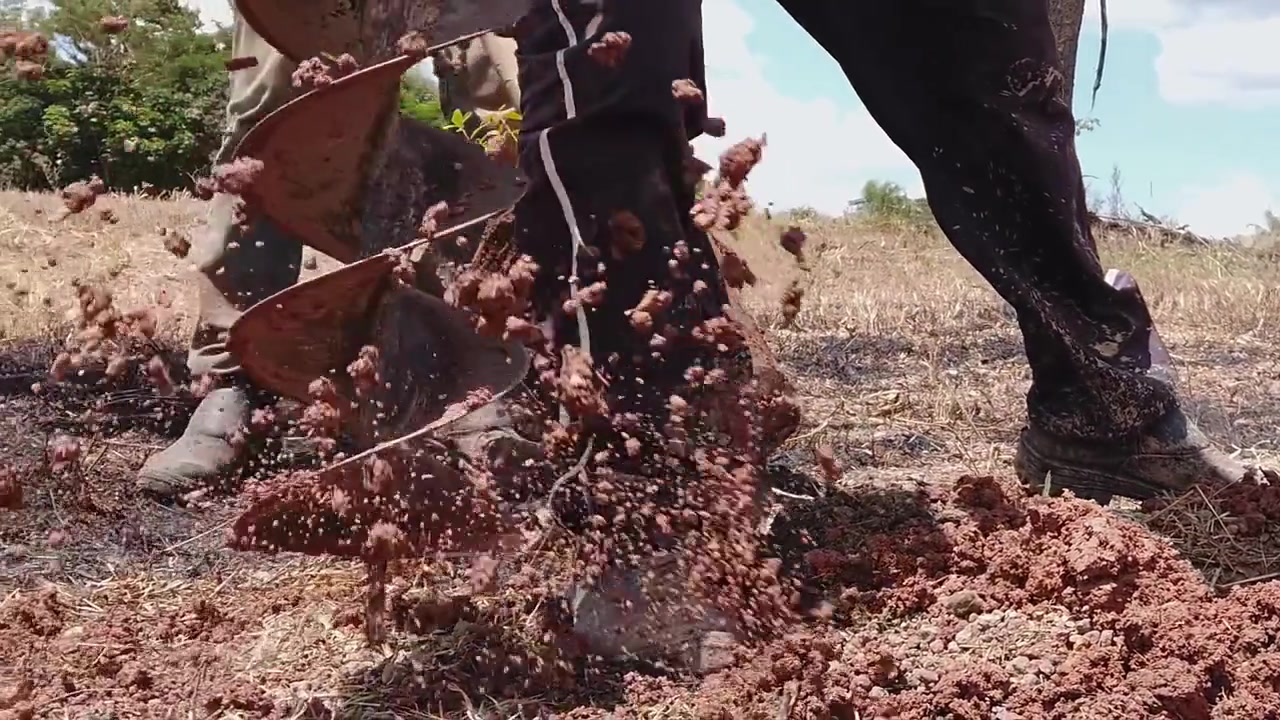 Primo piano di una trivella industriale che scava un foro profondo nel terreno per scopi edili o agricoli. La lama a spirale gira, smuovendo la terra