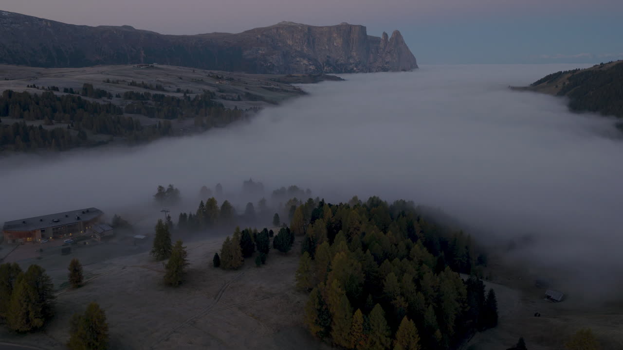 Cinematic aerial view of Sassolungo massif rising above a sea of clouds at sunrise, serene Alpe di Siusi alpine landscape in the Dolomites, Italian Alps travel destination