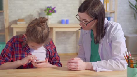 un médico psicólogo enseña a un niño autista a usar un teléfono inteligente de cerca