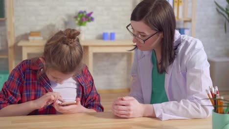 doctor psychologist teaches an autistic child to use a smartphone close up