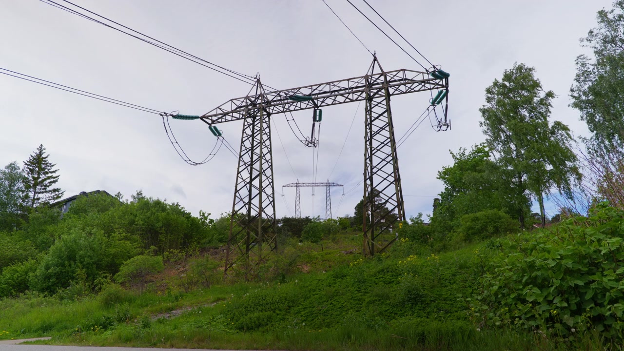 Power lines stretch across a lush hillside in Norway, framed by overcast skies. Ideal for themes of energy infrastructure or rural landscapes.