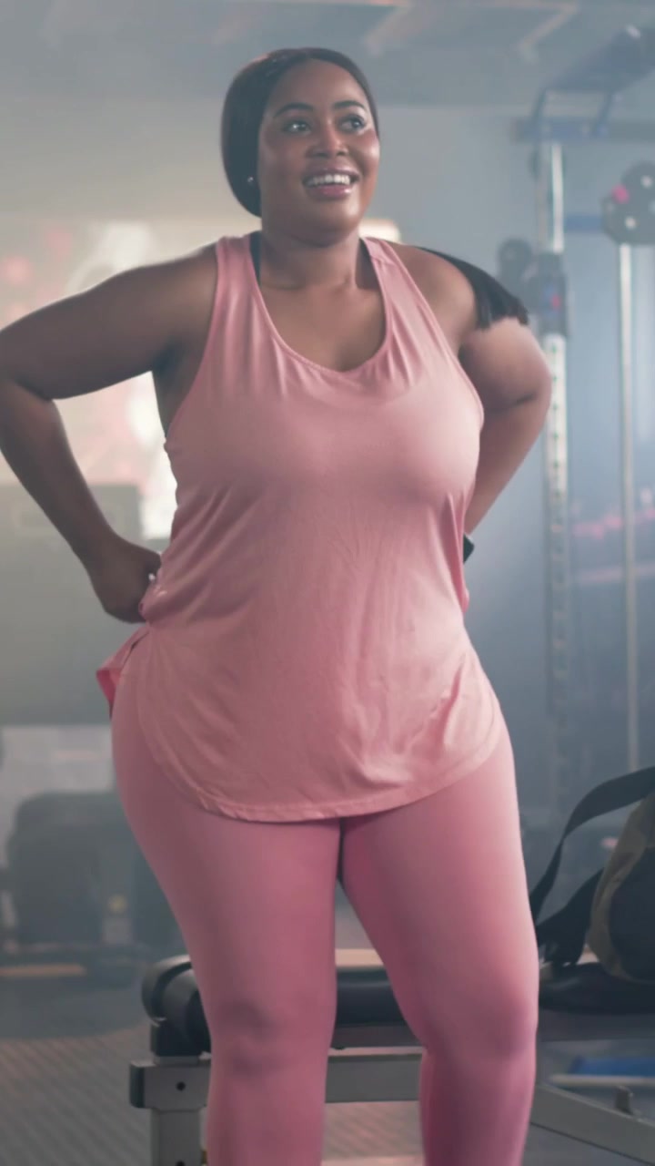 Video verticale: Una donna con un top rosa che entra da dietro, posiziona la borsa vicino a una panca da palestra e controlla lo shaker e l'orologio.