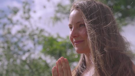 Close-up-of-white-woman,-smiling-with-hands-in-namaste-pose,-isolated-on-blurred-background