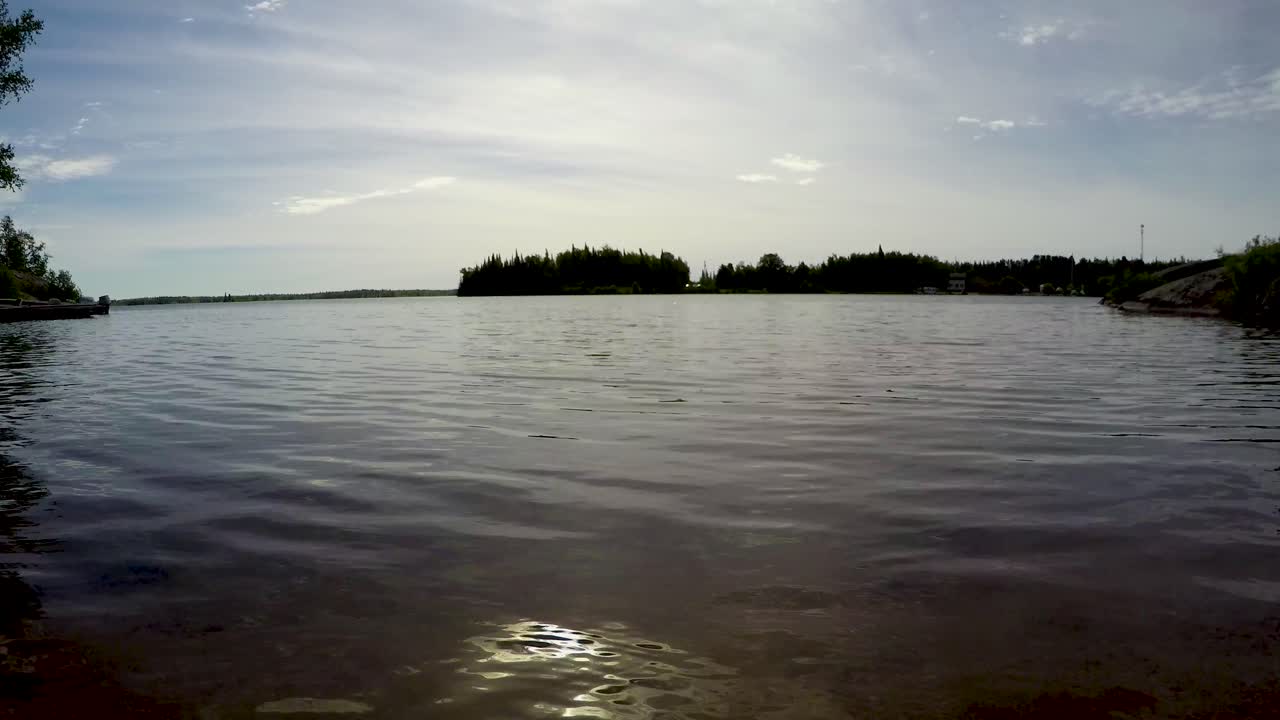 Lakeshore boreal forest time lapse low shot zoom out on sand beach of waves, boats and clouds in Point du Bois Manitoba Canada Whiteshell provincial park in the Great Canadian shield