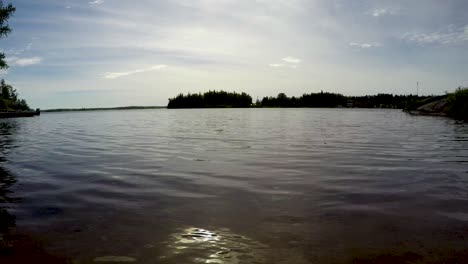 lakeshore boreal forest time lapse low shot zoom out on sand beach of waves, boats and clouds in point du bois manitoba canada whiteshell provincial park in the great canadian shield