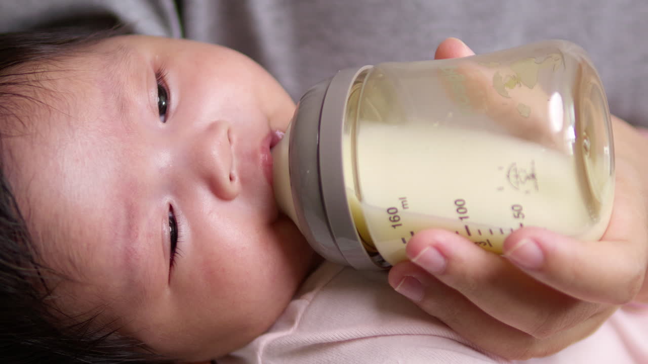 Cradling her newborn child in her arms while feeding her some formula milk in a plastic feeding bottle.