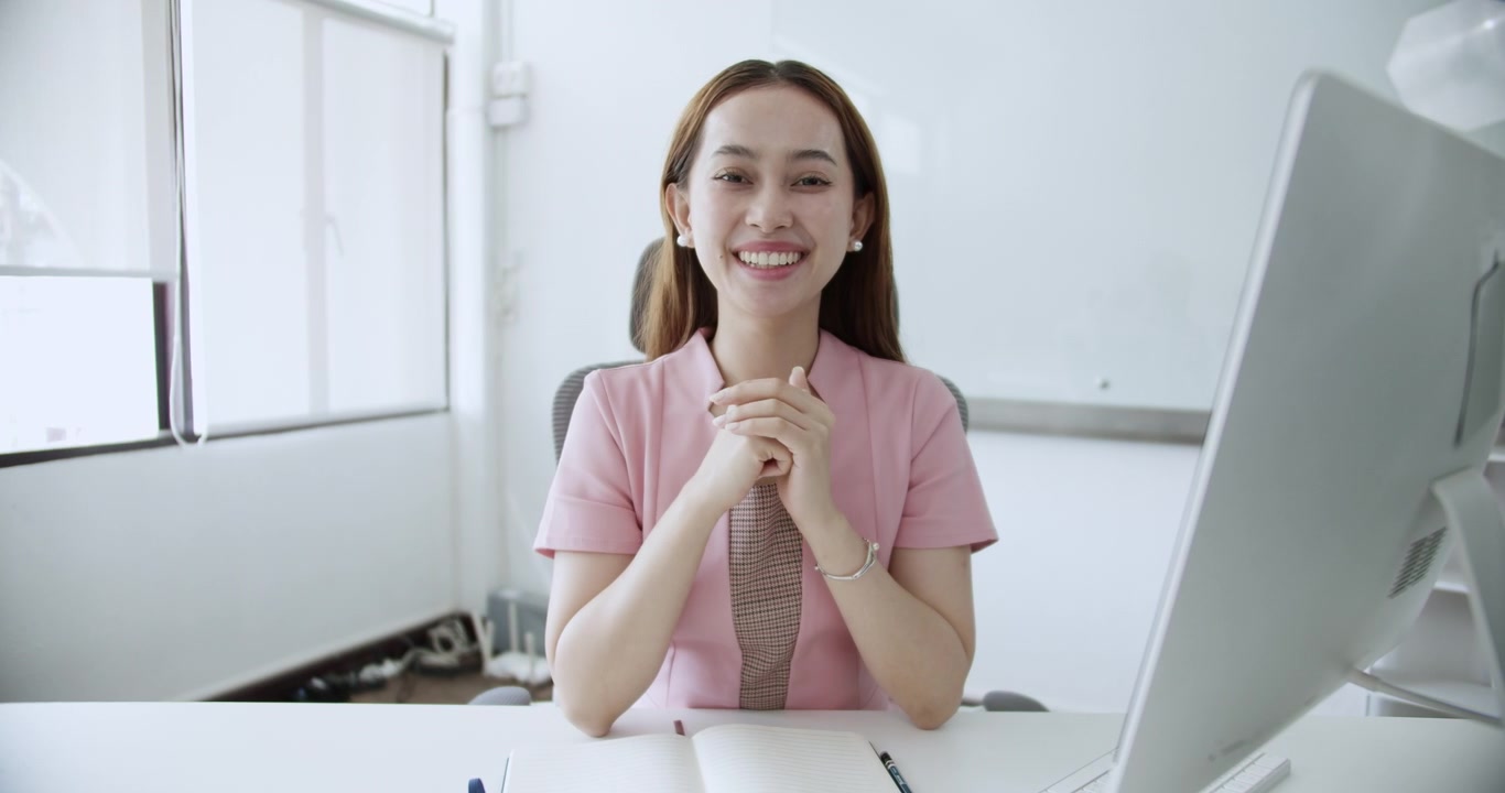 Un'impiegata allegra è seduta alla sua scrivania, saluta con la mano e sorride calorosamente. La sua energia positiva crea un'atmosfera di lavoro accogliente e professionale
