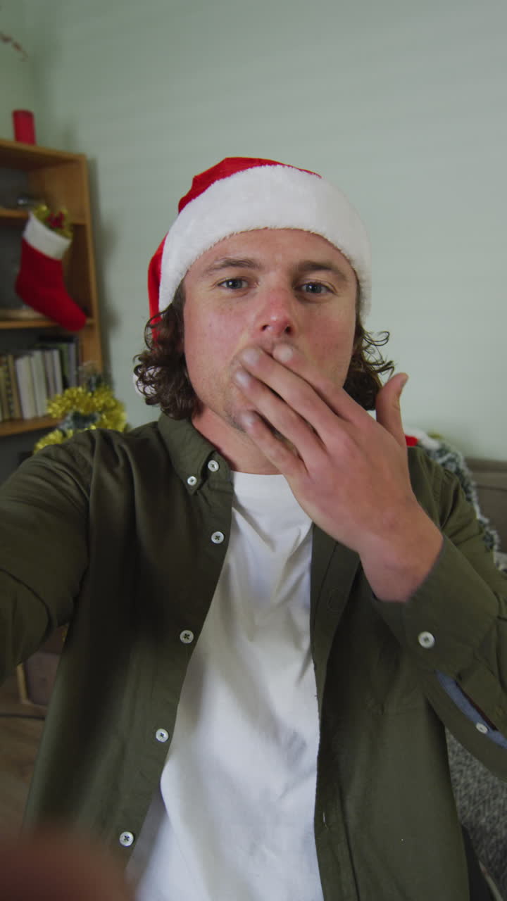 Vertical video of happy caucasian disabled man sitting in wheelchair wearing santa claus hat