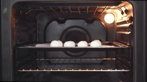 person opening a stove to put coconut rock buns inside then closing it back