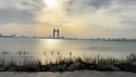 tracking shot of shanghai dishui lake at sunset, trees passing by in the foreground. bank of china jinrongzhongxin stands tall in the background,