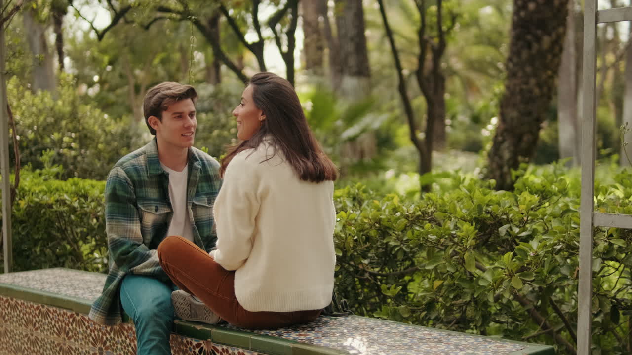 Happy young couple man and woman talking sitting in park