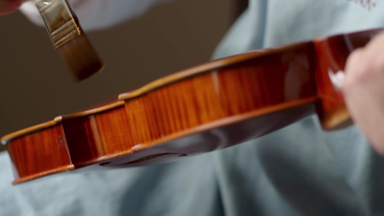 Skilled luthier brushing deep amber varnish onto handcrafted viola, highlighting intricate woodworking expertise in instrument making