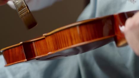 skilled luthier brushing deep amber varnish onto handcrafted viola, highlighting intricate woodworking expertise in instrument making