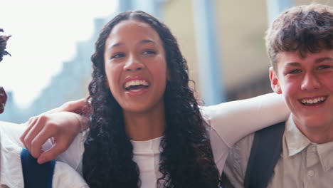 Close-Up-Portrait-Of-Smiling-Multi-Cultural-High-School-Or-Secondary-Pupils-Sitting-On-Wall-Outdoors