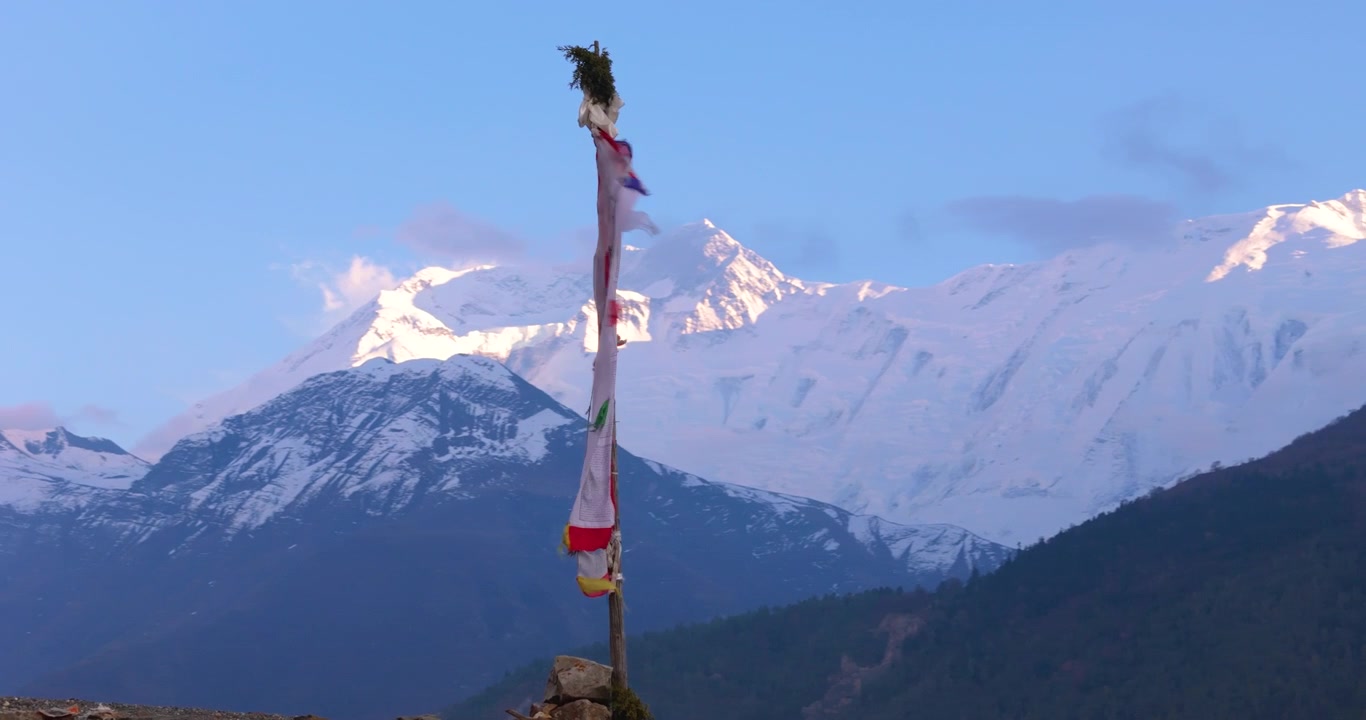 Circuito dell'Annapurna, Manang Nepal, ripresa aerea con drone di una bandiera di preghiera buddista verticale che sventola al vento su una collina con la cima innevata dell'Annapurna II sullo sfondo alla luce della sera