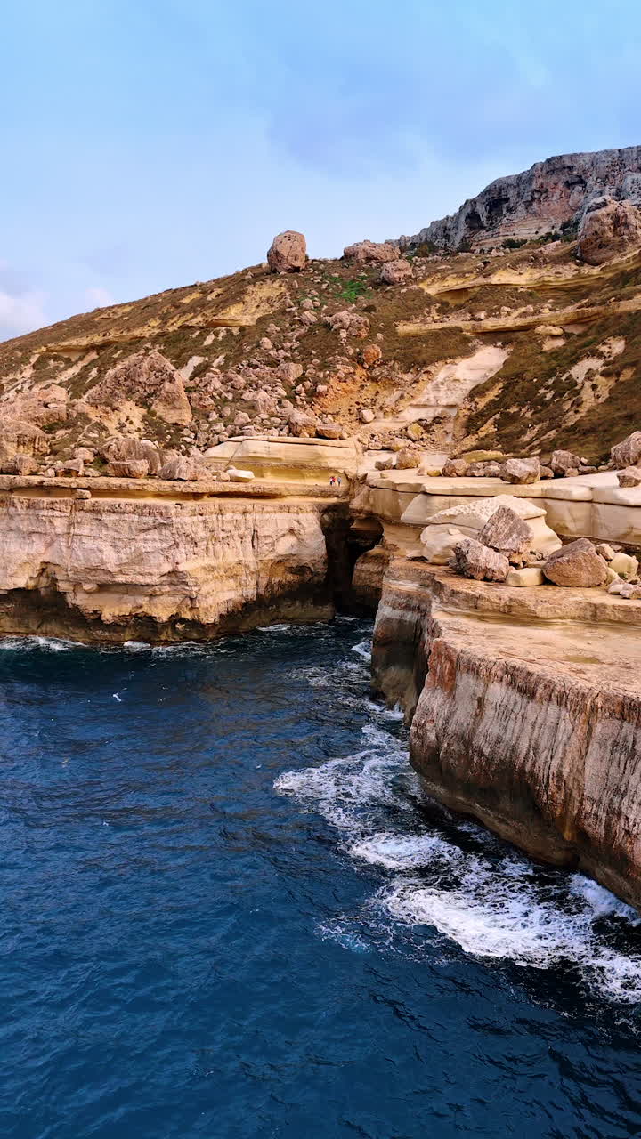 People stand on the edge of a high cliff. Drone footage distancing from the mount with seascape at the foot. Vertical video.