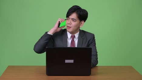 young handsome asian businessman working with laptop against green background