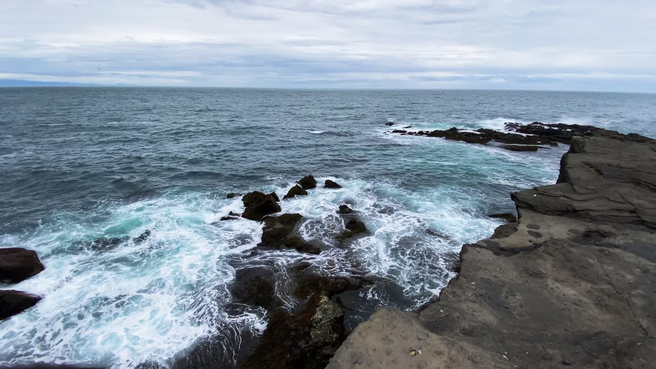 Pantai batu vulkanik di Islandia, ombak berbusa dalam gerak lambat.