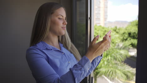 mujer feliz tomando una foto selfie con un teléfono celular junto a la ventana en casa