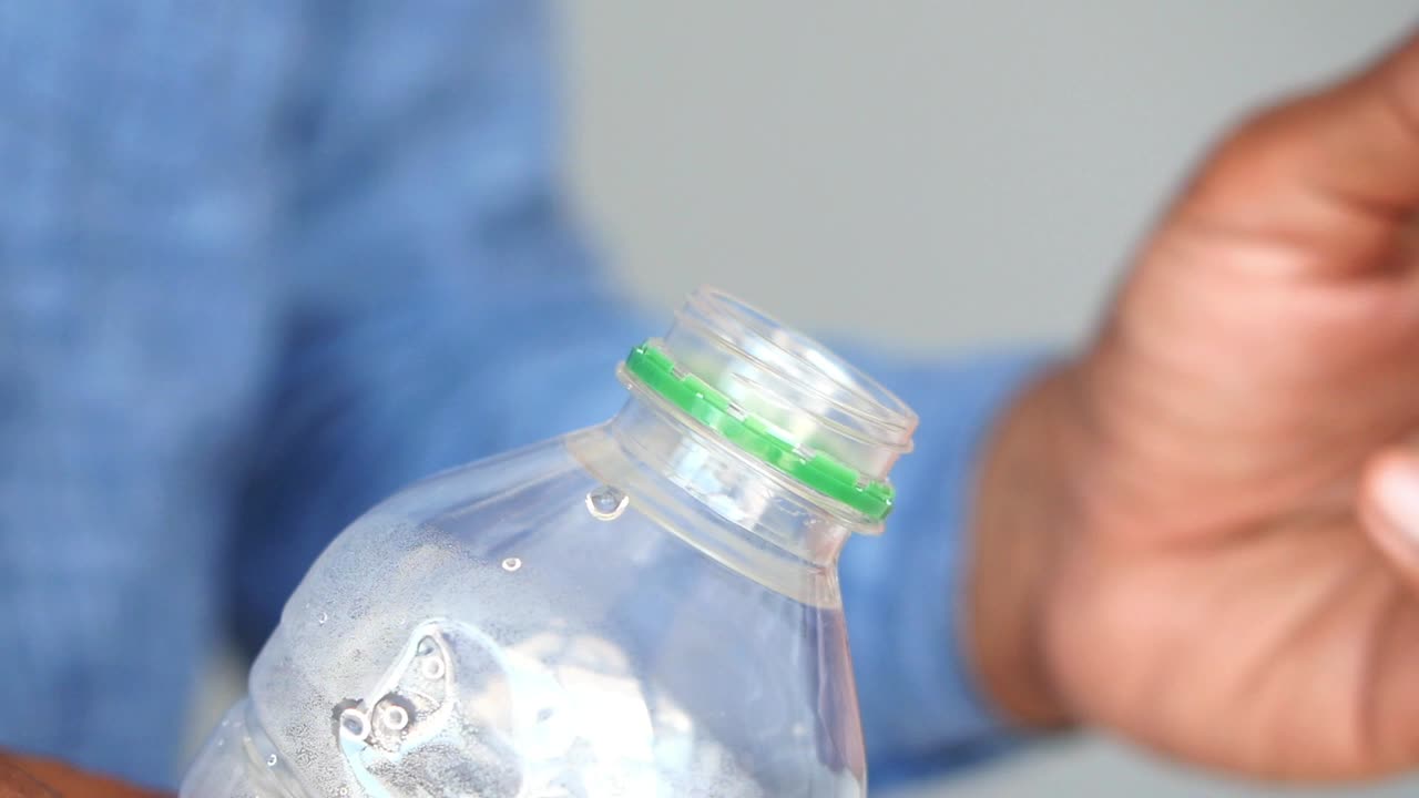 A close-up of a hand opening a plastic bottle with a green cap