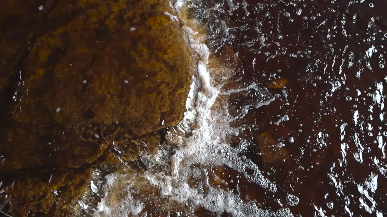 Top down view of clear abundant river water flowing over a stone boulder. Cold water flows over stone bottom showing the texture limestone structure, surface of the brown rock edge where water falls