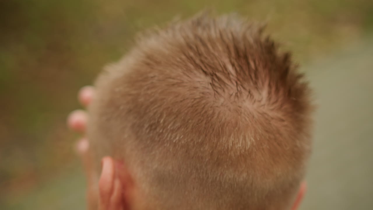 Primer plano de pelo mojado de un hombre caucásico en el exterior tocándose la cabeza con la mano, corte de pelo corto y puntiagudo peinado por la llovizna, sutiles gotas de lluvia en el cuero cabelludo, bokeh superficial con hojas de otoño de fondo, cinematográfico y melancólico
