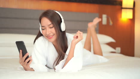 happy woman in bathrobe listening to music on the bed