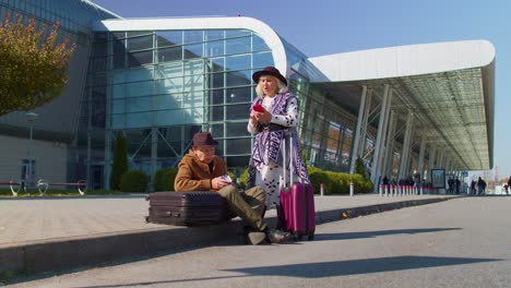 bored senior husband and wife retired tourists waiting for delayed boarding near airport terminal