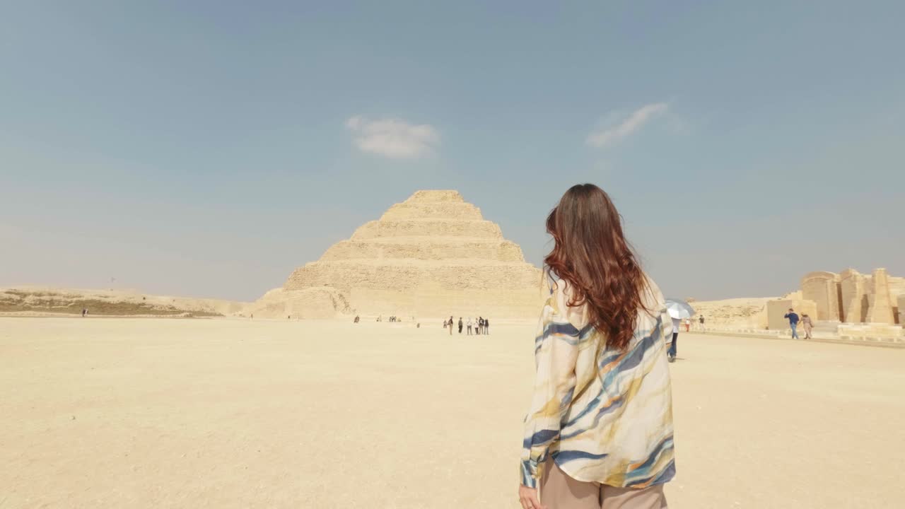 Donna che cammina verso l'antica piramide a gradoni nel deserto egiziano