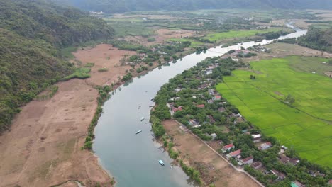 drone shot village by a blue river with green rice field half harvested